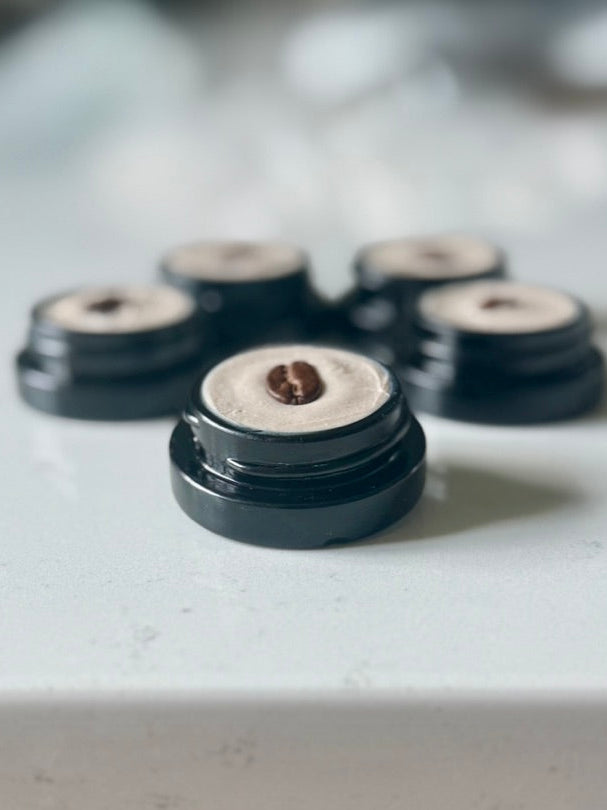 Close-up of coffee eye in a black container on a light surface. Inside the center of the coffee eye cream is one coffee bean