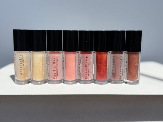 Row of lip gloss bottles with black caps on a light gray background